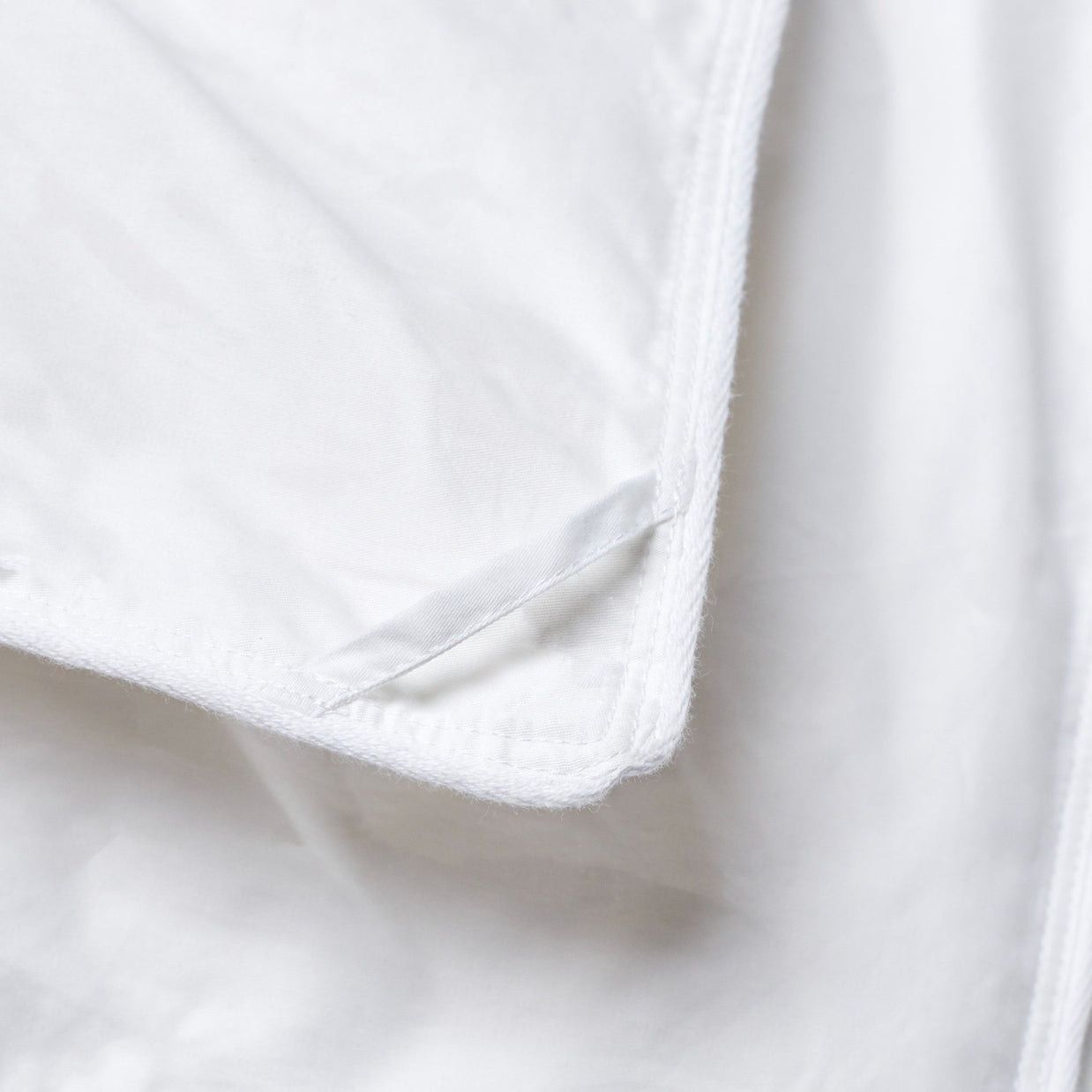 Detailed view of the white corner loop and stitching on a comforter, emphasizing secure construction and clean craftsmanship for duvet attachment.