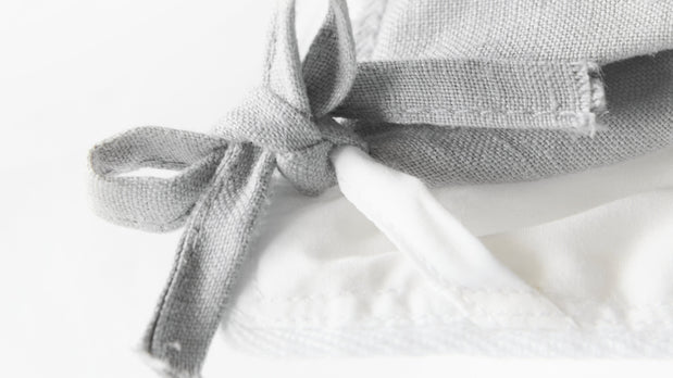 High-resolution close-up of a corner loop on an organic cotton comforter, highlighting the detailed stitching and secure attachment point for duvet covers.