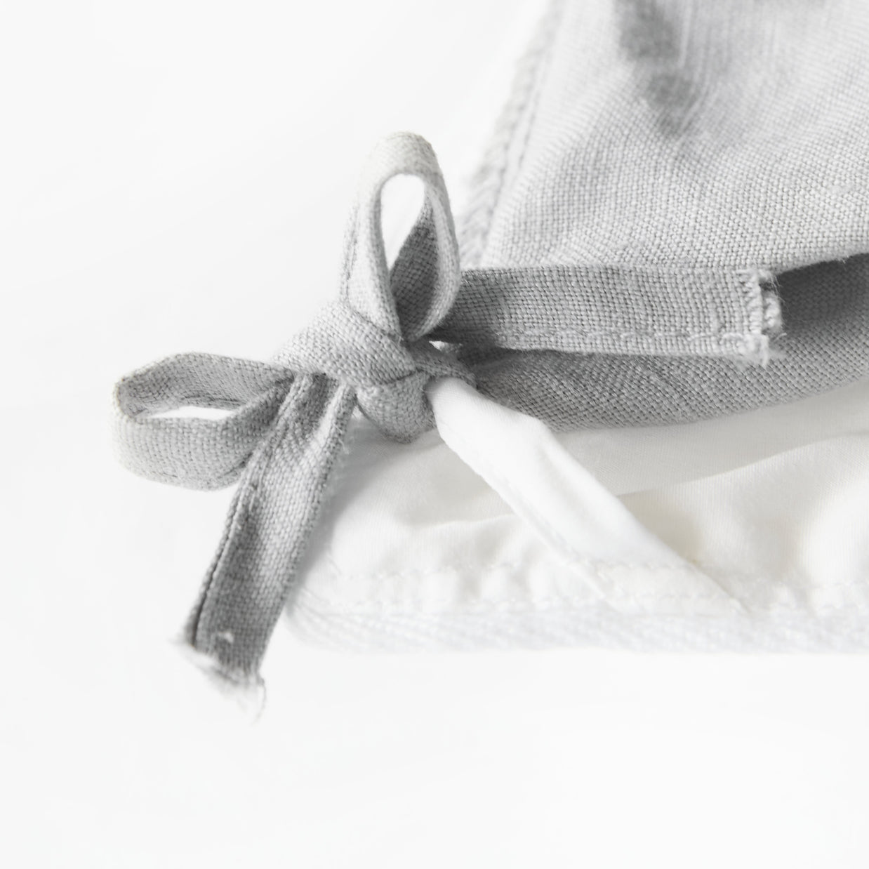 High-resolution close-up of a corner loop on an organic cotton comforter, highlighting the detailed stitching and secure attachment point for duvet covers.